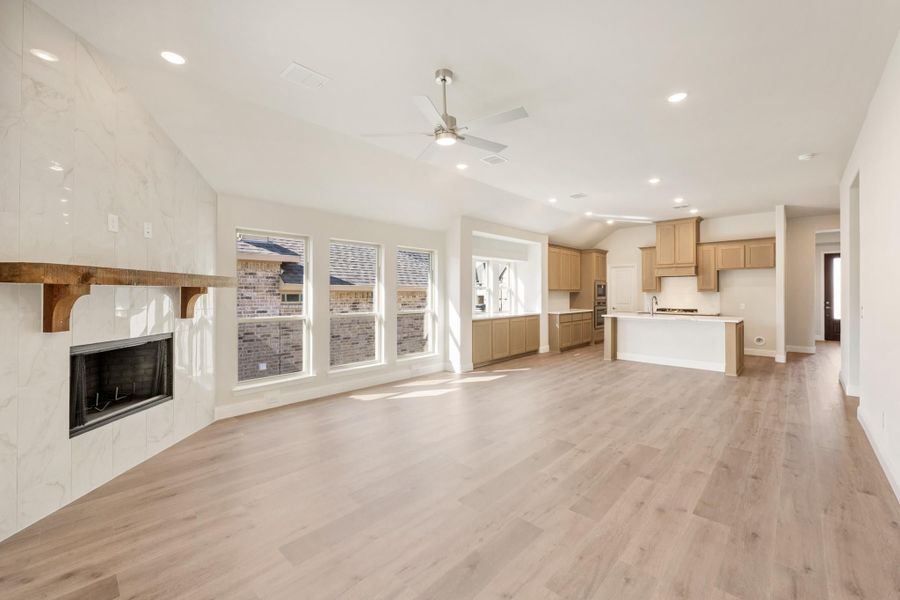 Open-concept living area with marble fireplace, hardwood floors, and kitchen with island and tan cabinets visible in background Open-concept living area with marble fireplace, hardwood floors, and kitchen with island and tan cabinets visible in background