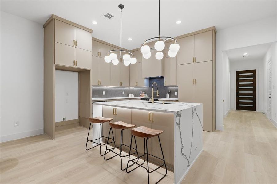 Modern kitchen featuring a waterfall island with a quartz countertop, sleek cabinetry with gold-tone hardware, and contemporary globe pendant lighting