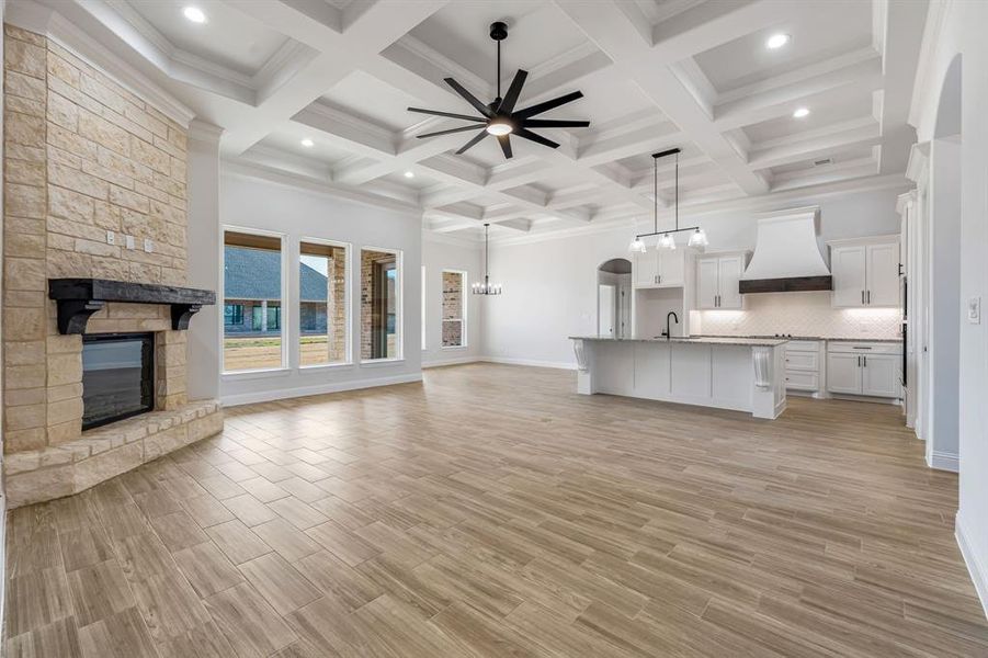 Unfurnished living room featuring ceiling fan with notable chandelier, a fireplace, coffered ceiling, and beamed ceiling