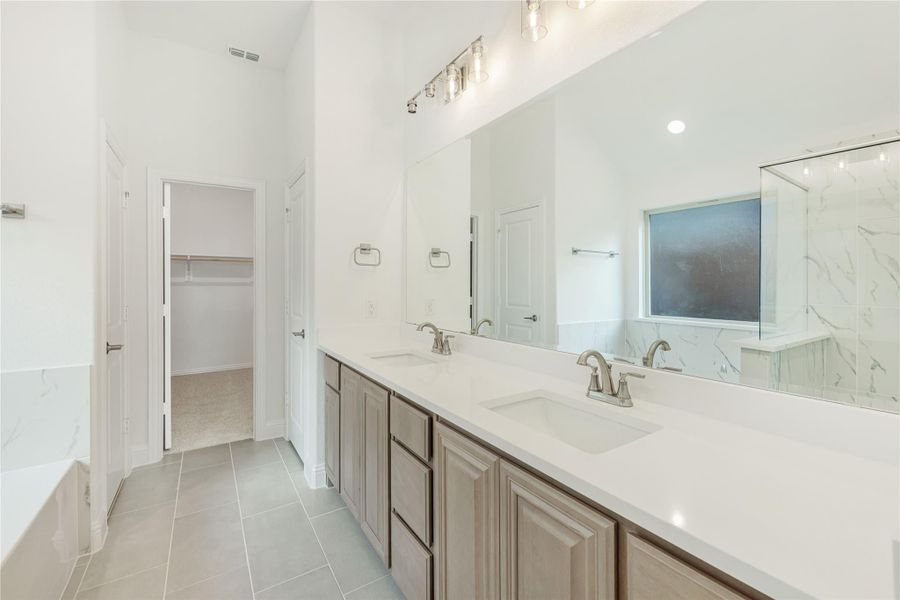 Master bathroom with double vanity, white countertops, soaking tub, and walk-in closet access