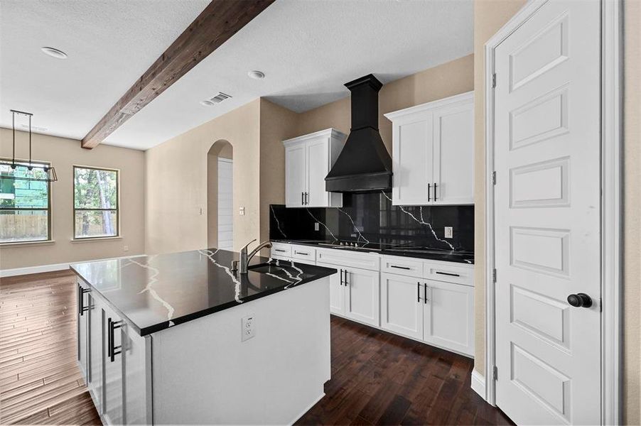 Kitchen with beamed ceiling, white cabinets, a kitchen island with sink, custom exhaust hood, and dark hardwood / wood-style flooring