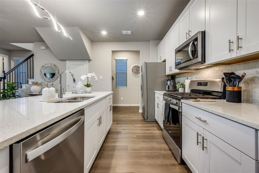 Kitchen with stainless steel appliances, light stone counters, white cabinets, light wood finished floors, and recessed lighting Kitchen with stainless steel appliances, light stone counters, white cabinets, light wood finished floors, and recessed lighting