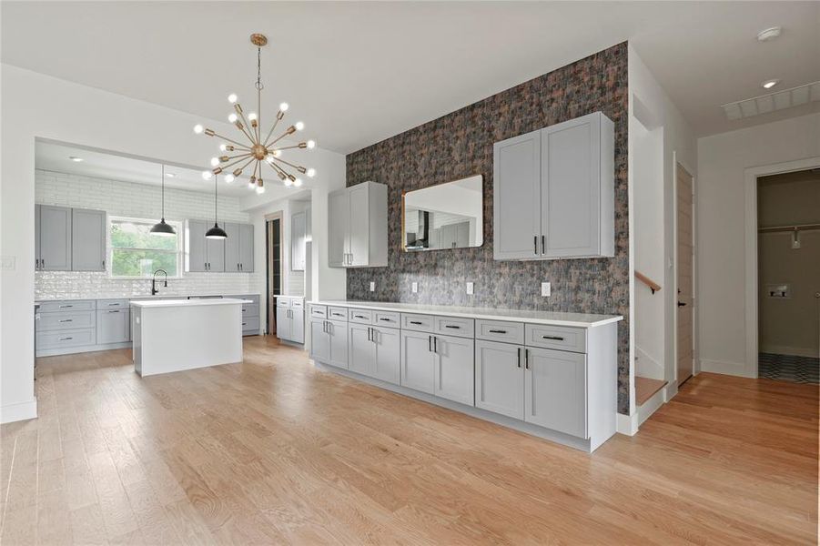 Kitchen with light wood-type flooring, tasteful backsplash, light countertops, a center island, and recessed lighting Kitchen with light wood-type flooring, tasteful backsplash, light countertops, a center island, and recessed lighting