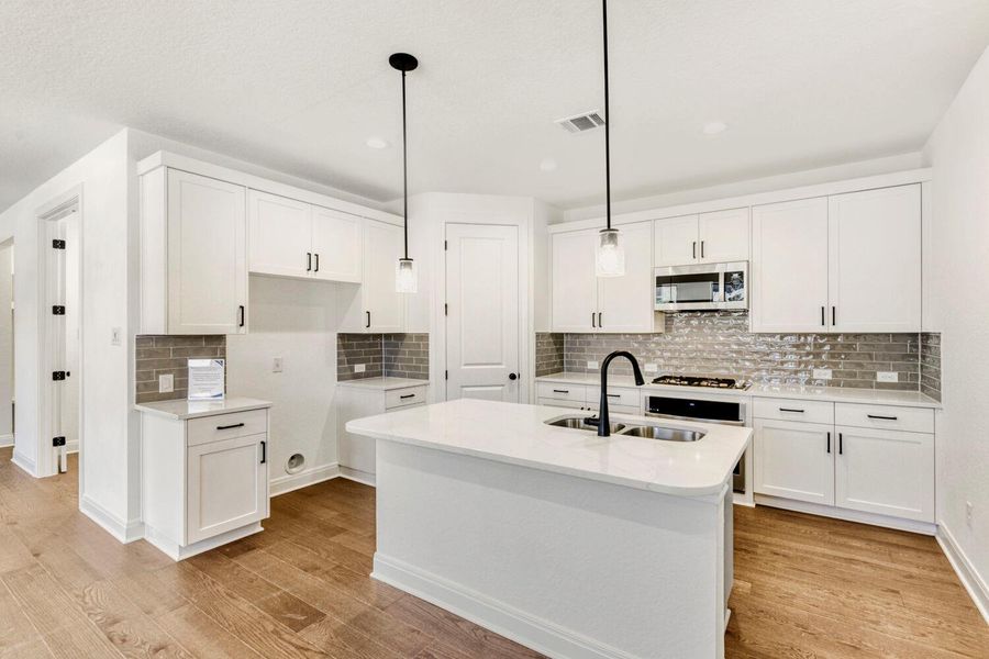 Kitchen with white cabinetry, light stone countertops, stainless steel microwave, and light wood finished floors Kitchen with white cabinetry, light stone countertops, stainless steel microwave, and light wood finished floors