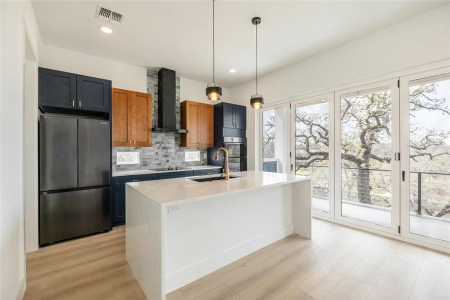 Two tone kitchen with stainless steel appliances, a kitchen island with sink, light stone counters, light wood-style floors, and two tone cabinetry