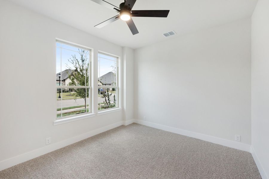 Empty bedroom with carpet flooring, ceiling fan, and two windows overlooking a neighborhood street