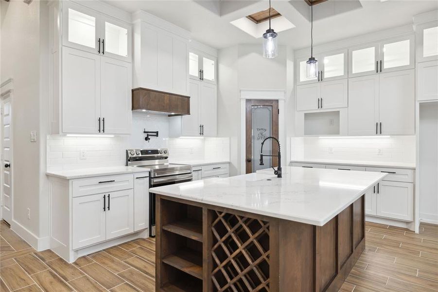 Kitchen featuring decorative light fixtures, a center island with sink, custom range hood, light stone countertops, and white cabinets