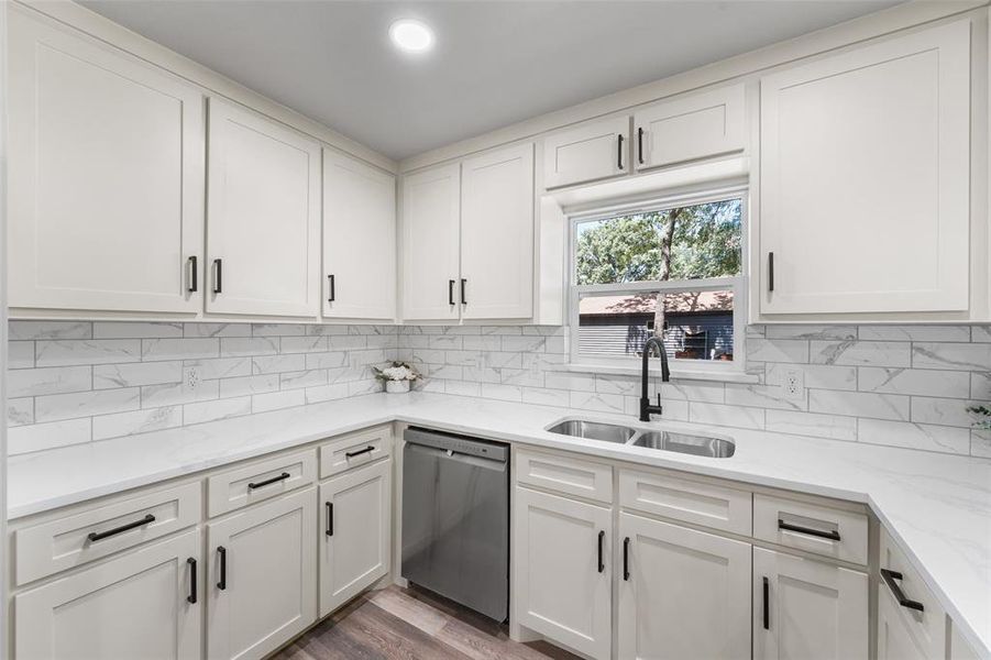 Modern kitchen featuring white shaker cabinetry, an undermount stainless steel double sink, a black gooseneck faucet, light-toned countertops, and a white subway tile backsplash with veining Modern kitchen featuring white shaker cabinetry, an undermount stainless steel double sink, a black gooseneck faucet, light-toned countertops, and a white subway tile backsplash with veining