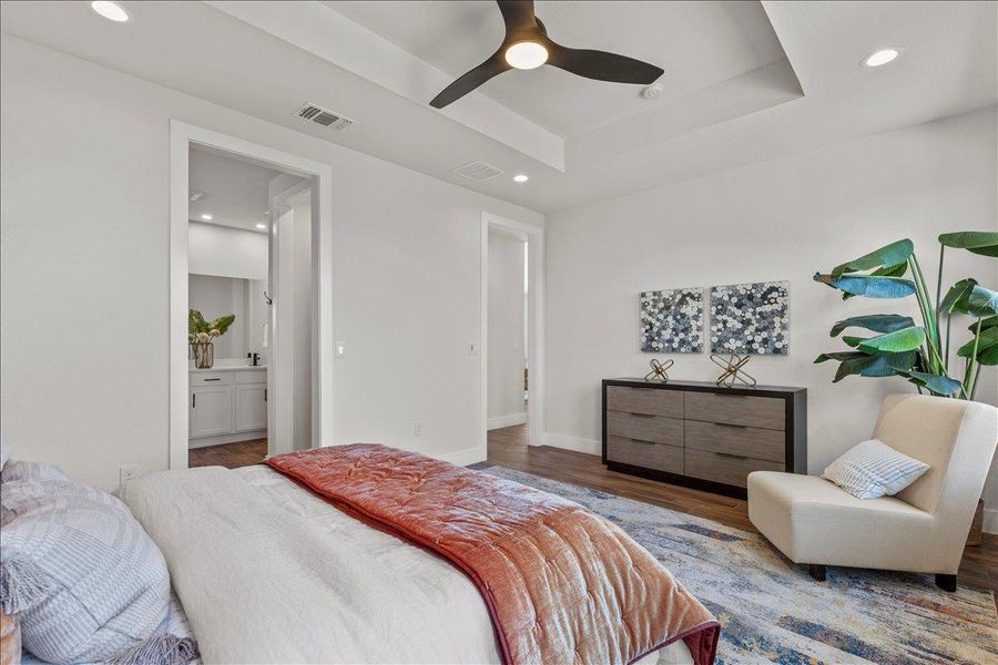 Bedroom with a tray ceiling, recessed lighting, wood finished floors, ceiling fan, and connected bathroom