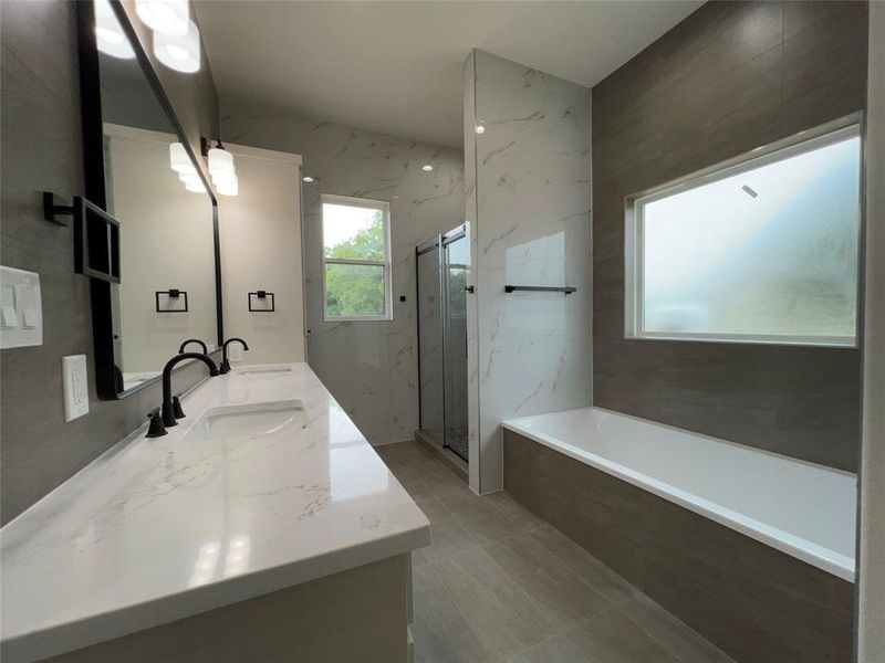 Modern bathroom featuring a double vanity with integrated sinks and black fixtures, a built-in soaking tub, and a separate glass-enclosed shower