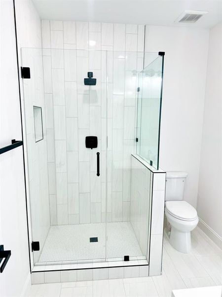 Bathroom featuring tile patterned flooring, toilet, and a shower with door