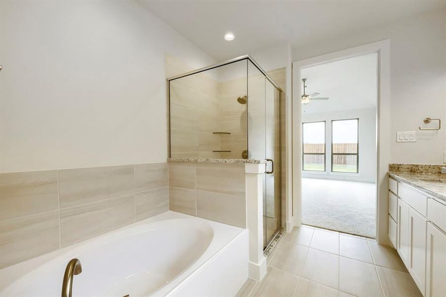 Soaking tub with bronze-finish fixtures, a glass-enclosed shower featuring tiled walls and built-in shelving, and a vanity with a stone countertop Soaking tub with bronze-finish fixtures, a glass-enclosed shower featuring tiled walls and built-in shelving, and a vanity with a stone countertop