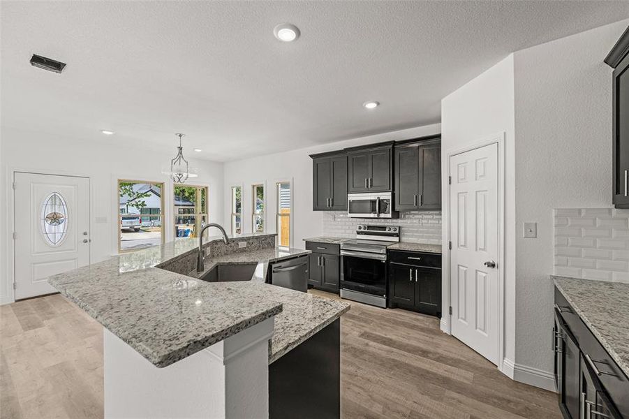 Kitchen with backsplash, a kitchen island with sink, appliances with stainless steel finishes, pendant lighting, and sink