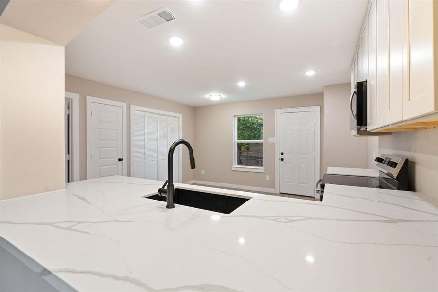 Kitchen with white cabinetry, stainless steel appliances, light stone counters, a peninsula, and recessed lighting