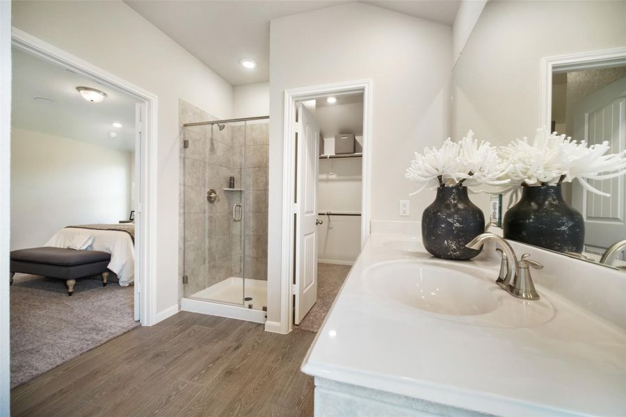 Escape to a spa-like oasis in this primary bathroom. Enjoy a walk-in shower with tile surround, a separate garden tub with custom detailing, and an elegant vanity featuring light countertops, modern hardware, and beautiful vanity lights. Experience luxury and relaxation in every detail. Sample photo of completed home with similar floor plan. Actual colors and selections may vary.