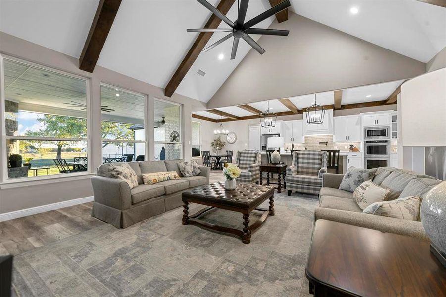 Living room featuring beamed ceiling, ceiling fan with notable chandelier, hardwood / wood-style flooring, and high vaulted ceiling