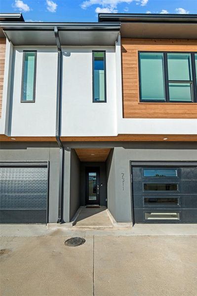 Front Exterior features a covered entry with wood-paneled ceiling accent. Black front door includes a glass insert providing natural light. Garage door features horizontal glass panels positioned below the address numbers.