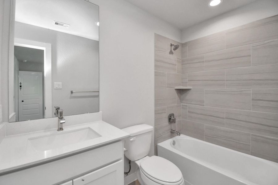 Secondary bath features tile flooring, bath/shower combo with tile surround, light stained wood cabinets, beautiful light countertop.
