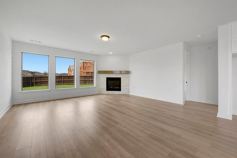 Spacious room with wood-finish flooring, a corner fireplace with a stone surround and wood mantel, and three large windows overlooking a fenced backyard