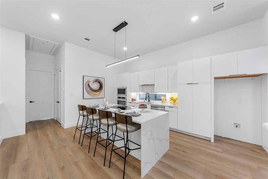 Kitchen with white cabinets, tasteful backsplash, a kitchen breakfast bar, modern cabinets, and decorative light fixtures Kitchen with white cabinets, tasteful backsplash, a kitchen breakfast bar, modern cabinets, and decorative light fixtures