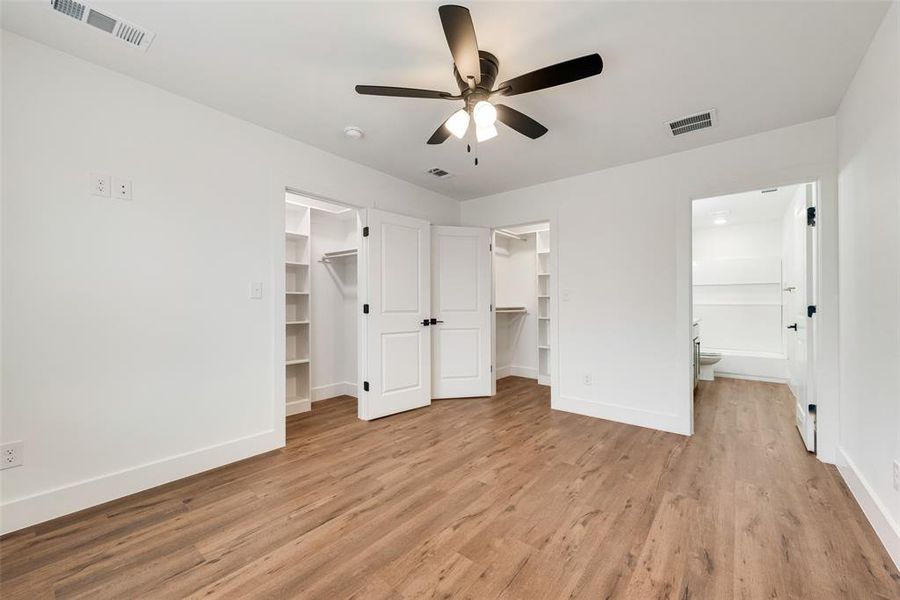 Unfurnished bedroom with connected bathroom, a walk in closet, ceiling fan, light wood-type flooring, and a closet