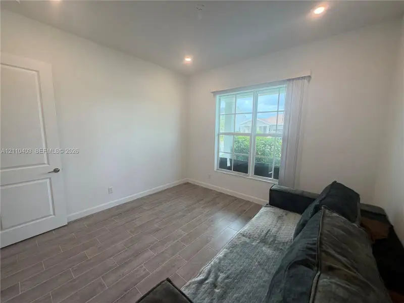 Neutral-toned interior featuring wood-finish tile flooring, recessed ceiling lighting, a multi-pane window, and a paneled interior door