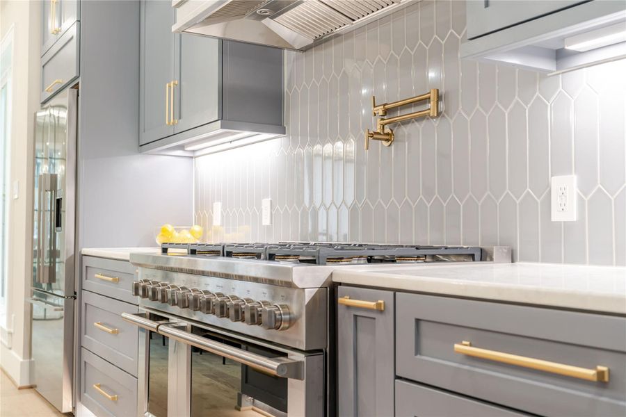 Kitchen with slate blue cabinetry, under cabinet lighting, high end appliances, decorative backsplash, and light stone countertops