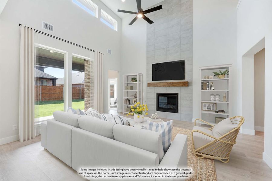 Living room with two-story ceiling, tile fireplace, ceiling fan, and large windows overlooking backyard
