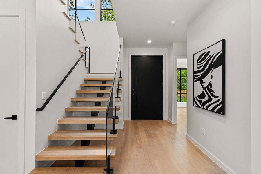 A modern floating staircase anchors the light-filled entrance foyer with warm hardwood floors.