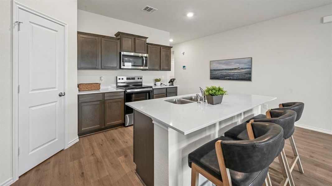 Kitchen with stainless steel appliances, an island with sink, dark brown cabinets, a breakfast bar area, and dark wood finished floors Kitchen with stainless steel appliances, an island with sink, dark brown cabinets, a breakfast bar area, and dark wood finished floors