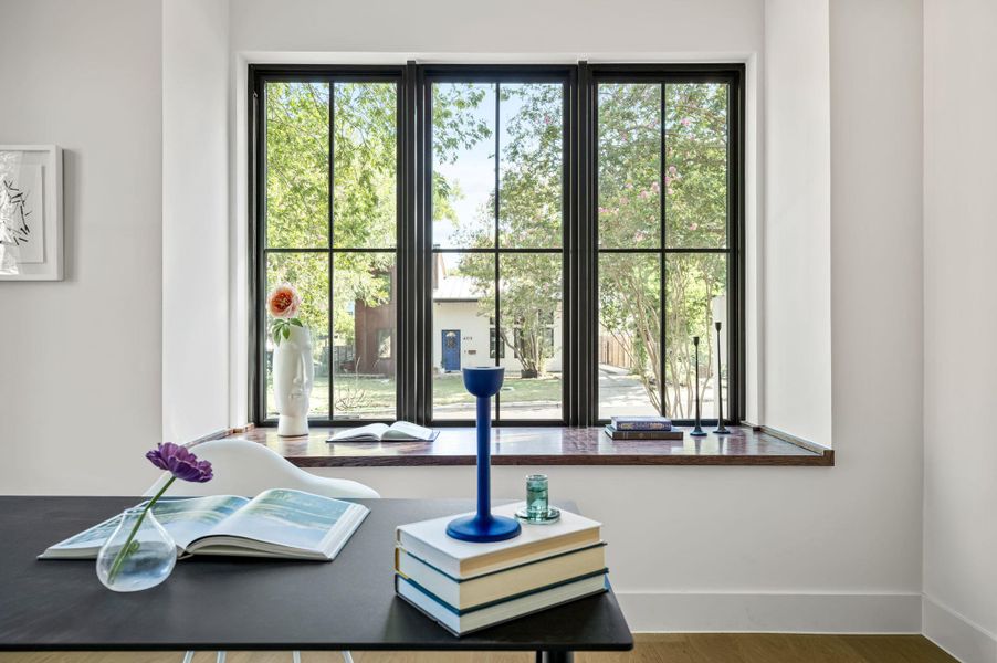 A well-lit study area features a wide window overlooking a verdant outdoor landscape.