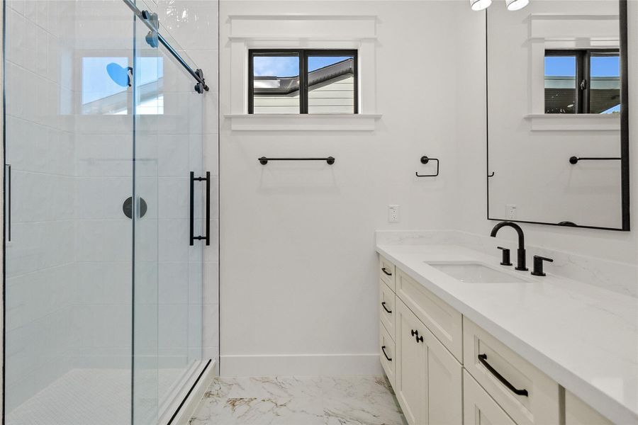 A beautifully finished secondary bathroom features a sleek glass-enclosed shower, quartz vanity, and timeless designer finishes.