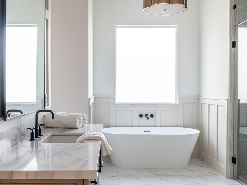Full bathroom featuring vanity, light marble finish floors, a soaking tub, a decorative wall, and a wainscoted wall
