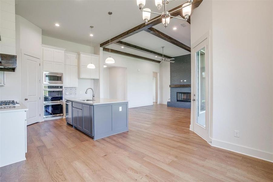 Kitchen with beamed ceiling, light hardwood / wood-style flooring, an island with sink, and stainless steel appliances