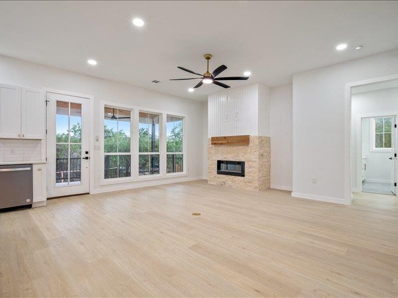 Spacious living area featuring light-toned flooring, a fireplace with a stone surround and wood mantel, large windows with views of trees, and recessed lighting