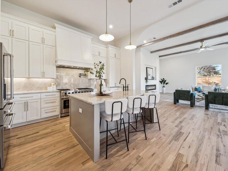 Kitchen featuring white cabinets, appliances with stainless steel finishes, custom range hood, and an island with sink