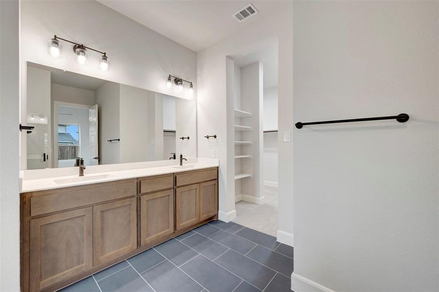Bathroom featuring double vanity, a walk in closet, dark tile patterned flooring, and built in features