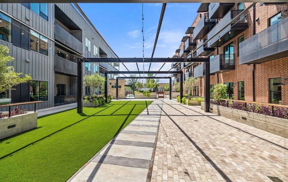 A spacious central courtyard features paved walkways, manicured turf, and an overhead architectural trellis framework. A spacious central courtyard features paved walkways, manicured turf, and an overhead architectural trellis framework.