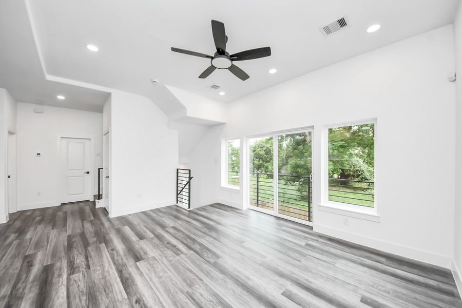 This modern living area features sleek vinyl flooring, large windows for ample natural light, and a ceiling fan. The space opens to a balcony with outdoor views, creating a bright and airy atmosphere. This modern living area features sleek vinyl flooring, large windows for ample natural light, and a ceiling fan. The space opens to a balcony with outdoor views, creating a bright and airy atmosphere.