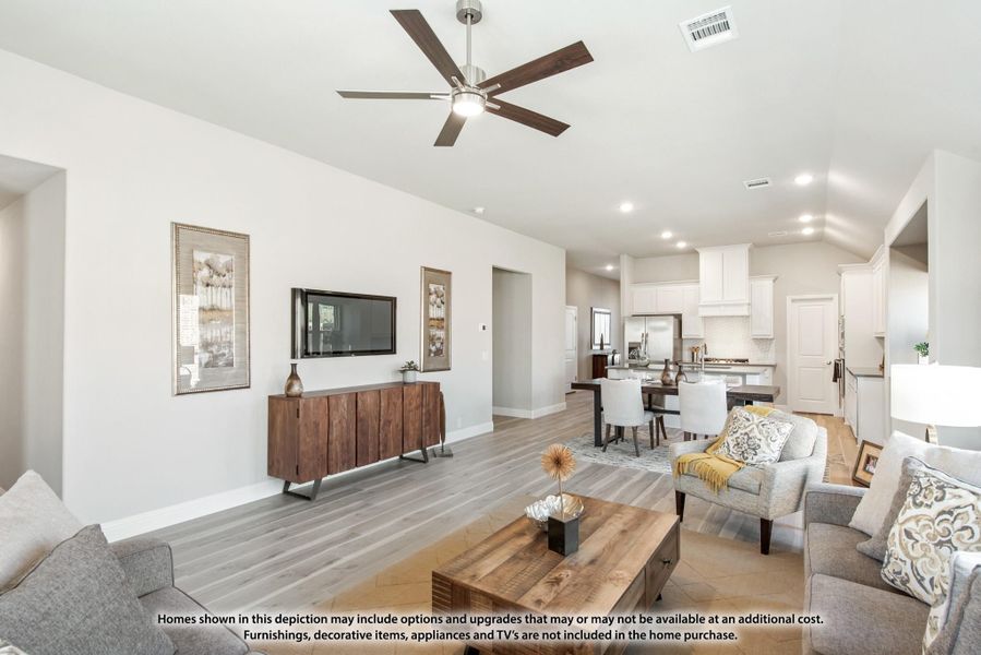 Open-concept living room with vaulted ceiling, ceiling fan, hardwood floors, and kitchen visible in background. Open-concept living room with vaulted ceiling, ceiling fan, hardwood floors, and kitchen visible in background.