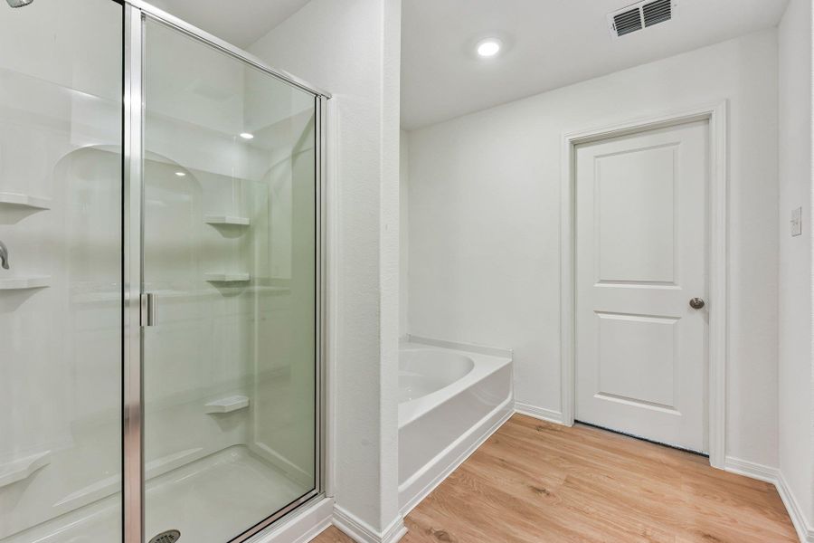 Full bathroom featuring a glass-enclosed shower with integrated shelving, a built-in bathtub, wood-finish flooring, a white paneled door, and recessed lighting