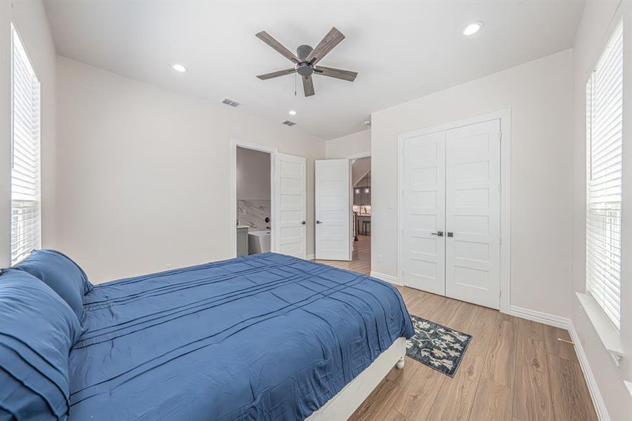 Bedroom featuring multiple windows, light wood finished floors, ensuite bath, a ceiling fan, and recessed lighting Bedroom featuring multiple windows, light wood finished floors, ensuite bath, a ceiling fan, and recessed lighting