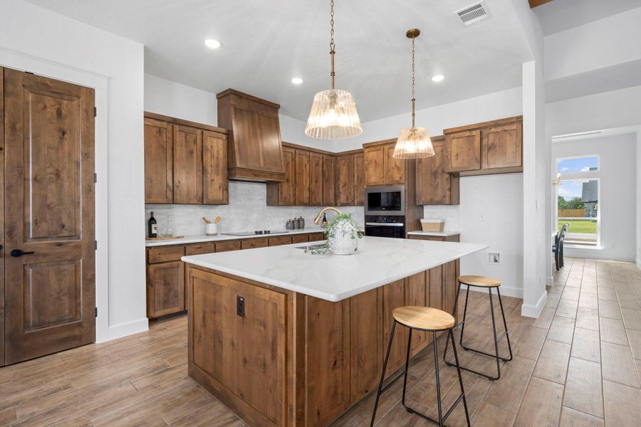 Kitchen featuring wood tiled floors, a breakfast bar, a center island with sink, light stone countertops, and tasteful backsplash