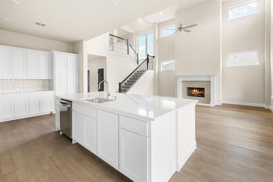 Kitchen featuring a fireplace, an island with sink, sink, dishwasher, and light hardwood / wood-style floors