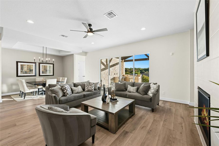 Living room featuring a tile fireplace, light wood-type flooring, ceiling fan, recessed lighting, and a tray ceiling Living room featuring a tile fireplace, light wood-type flooring, ceiling fan, recessed lighting, and a tray ceiling