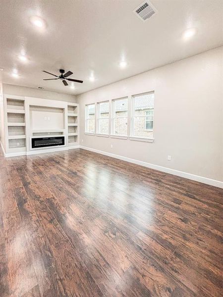 Unfurnished living room featuring built in shelves, a glass covered fireplace, dark wood-style flooring, a ceiling fan, and recessed lighting Unfurnished living room featuring built in shelves, a glass covered fireplace, dark wood-style flooring, a ceiling fan, and recessed lighting