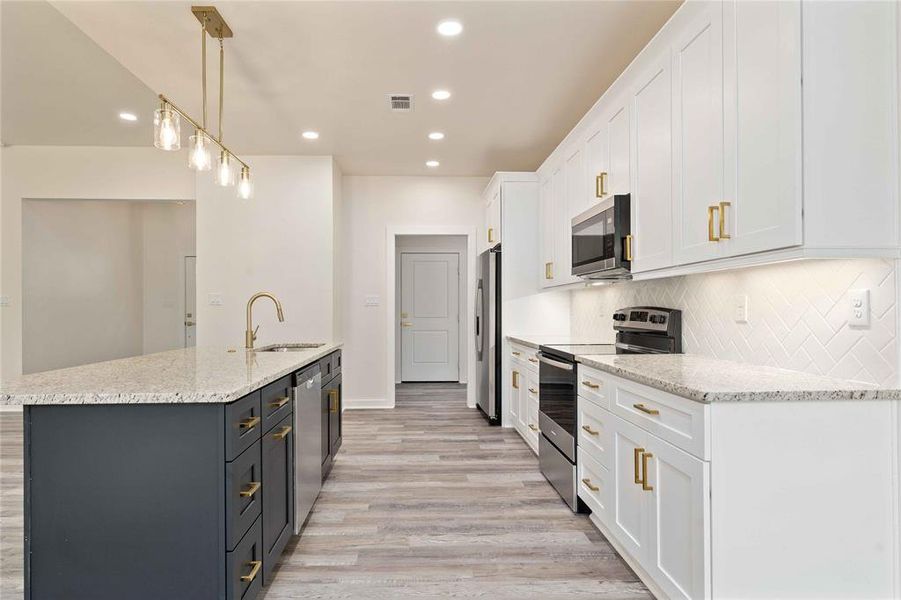 Kitchen featuring white cabinets, decorative light fixtures, appliances with stainless steel finishes, light stone countertops, and recessed lighting Kitchen featuring white cabinets, decorative light fixtures, appliances with stainless steel finishes, light stone countertops, and recessed lighting