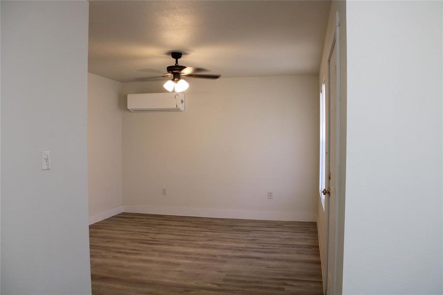 Empty room featuring wood finished floors, a ceiling fan, and a wall mounted AC