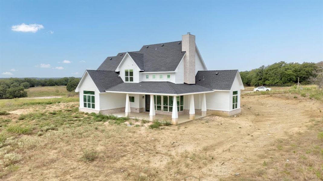 Rear view of property featuring a shingled roof, a patio area, a chimney, and dirt driveway Rear view of property featuring a shingled roof, a patio area, a chimney, and dirt driveway