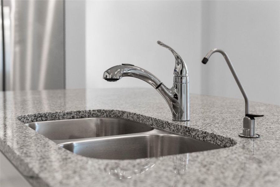 This modern kitchen island features a polished granite countertop with an undermount double-bowl stainless steel sink, complemented by a Moen Integra chrome kitchen faucet and a dedicated reverse osmosis drinking water tap.